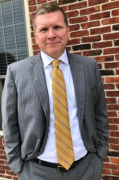 Jason L. McAuley, attorney, in a grey suit and gold tie in front of a brick wall